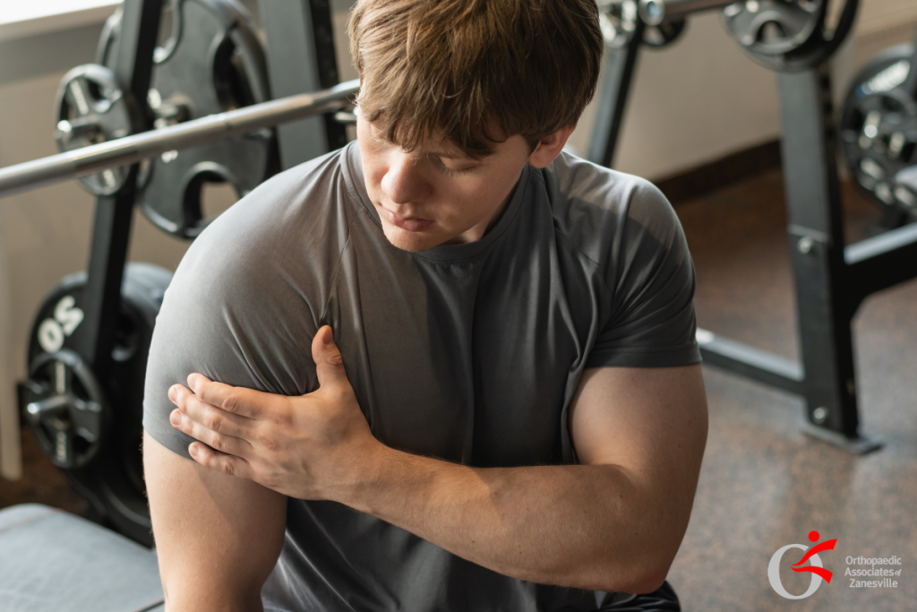 A male weightlifter gripping his painful right shoulder in a gym, experiencing deep joint pain from a Glenoid Chondral Defect in Zanesville, Ohio.